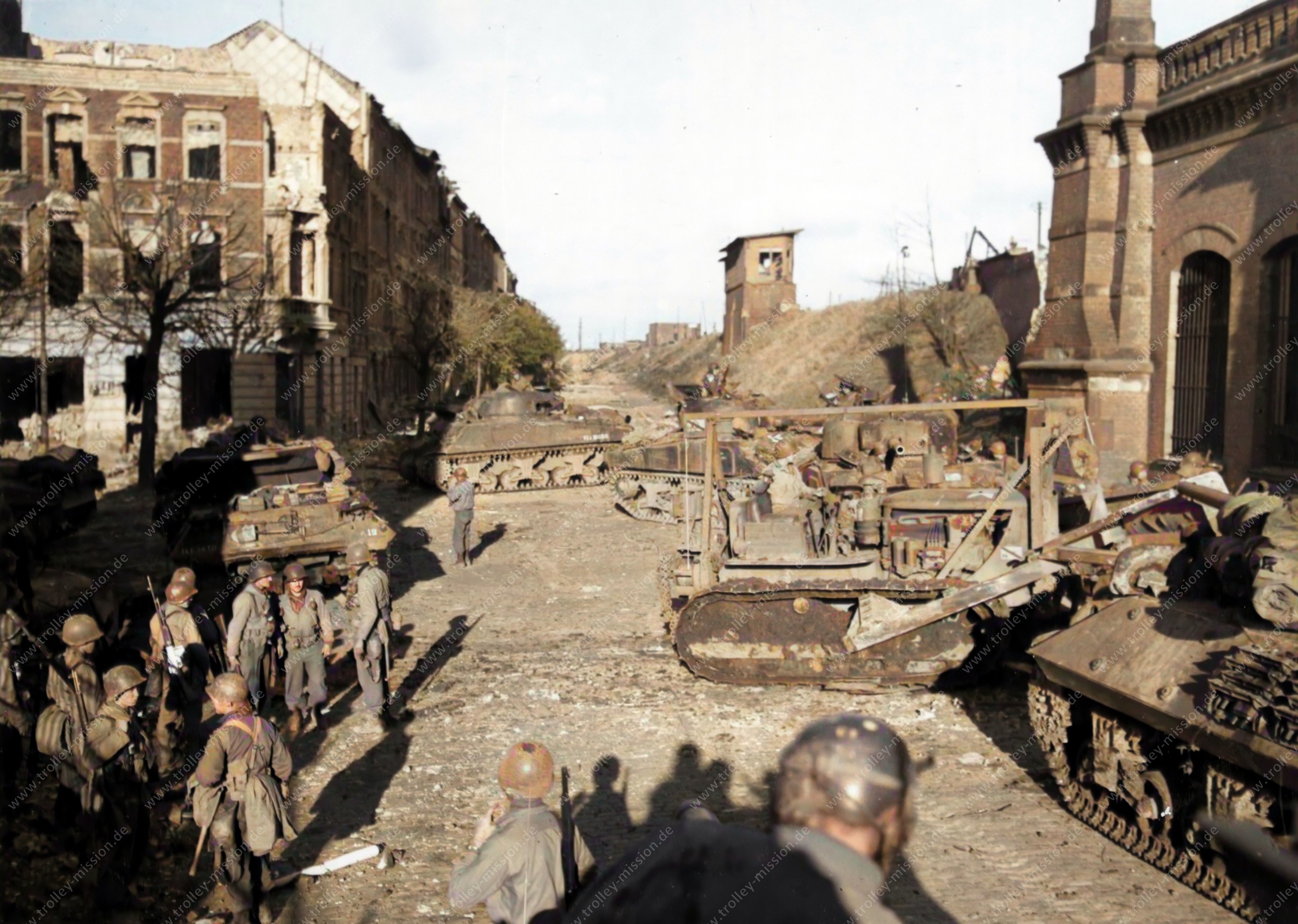 Die Soldaten der US Armee versammeln sich auf dem heutigen Hansa Platz. Im Hintergrund sind die zerstörten Wohnhäuser entlang des Reichsweges in Aachen zu erkennen.